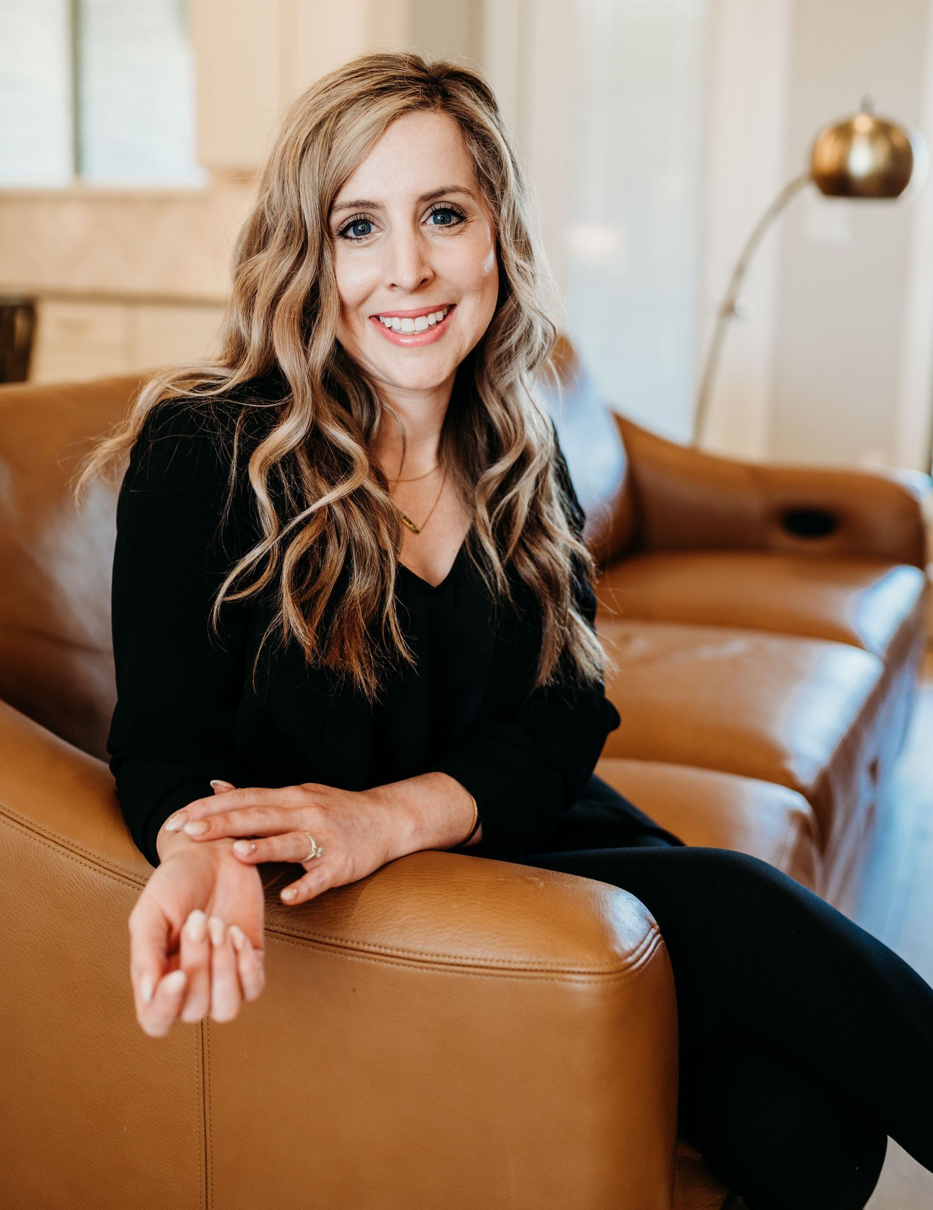 A woman is sitting on a brown leather couch and smiling.