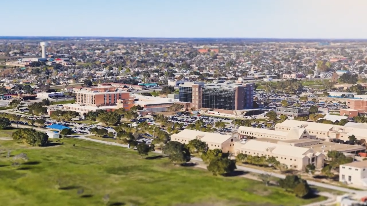 Aerial view of a sprawling city with low-rise buildings, roads, and green fields under a clear sky