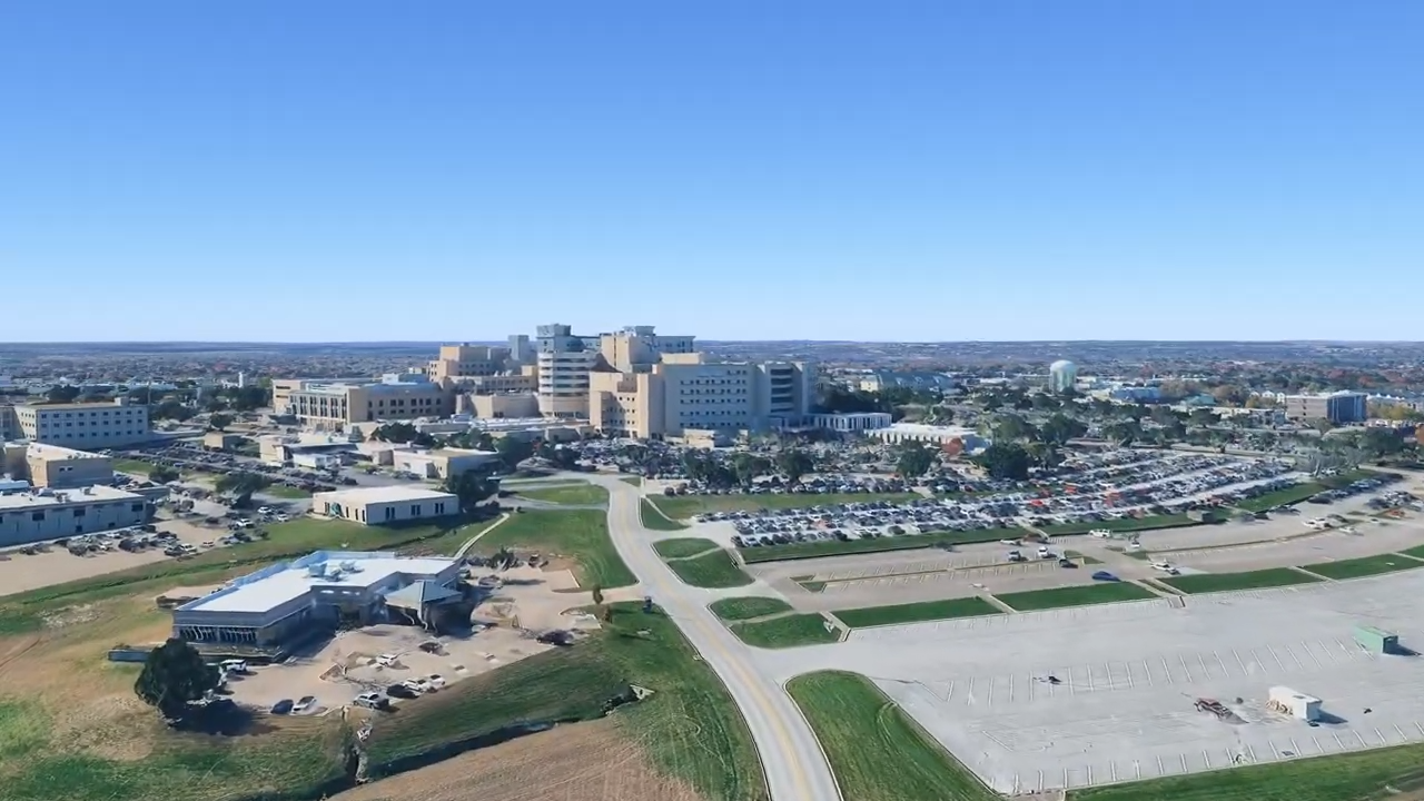 An aerial view of a large complex of buildings, parking lots, and open land under a clear blue sky.