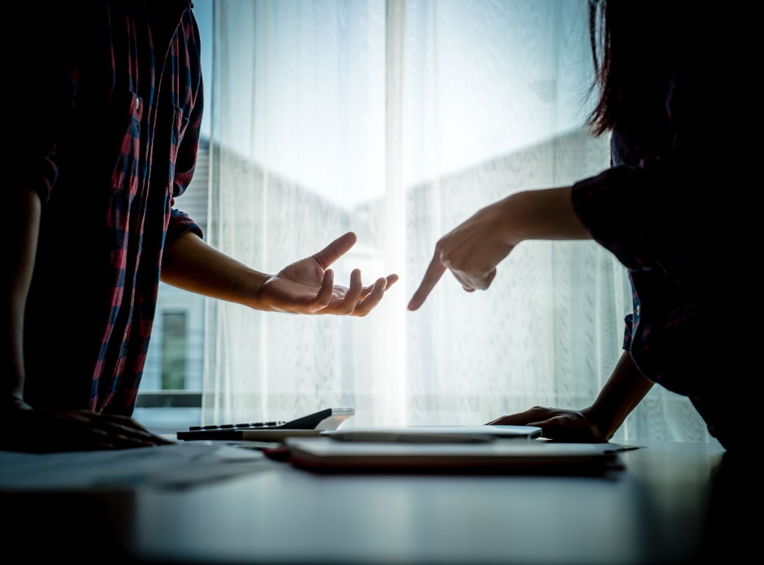 Two people gesturing over a tablet on a desk; one points, the other gestures open-handedly.