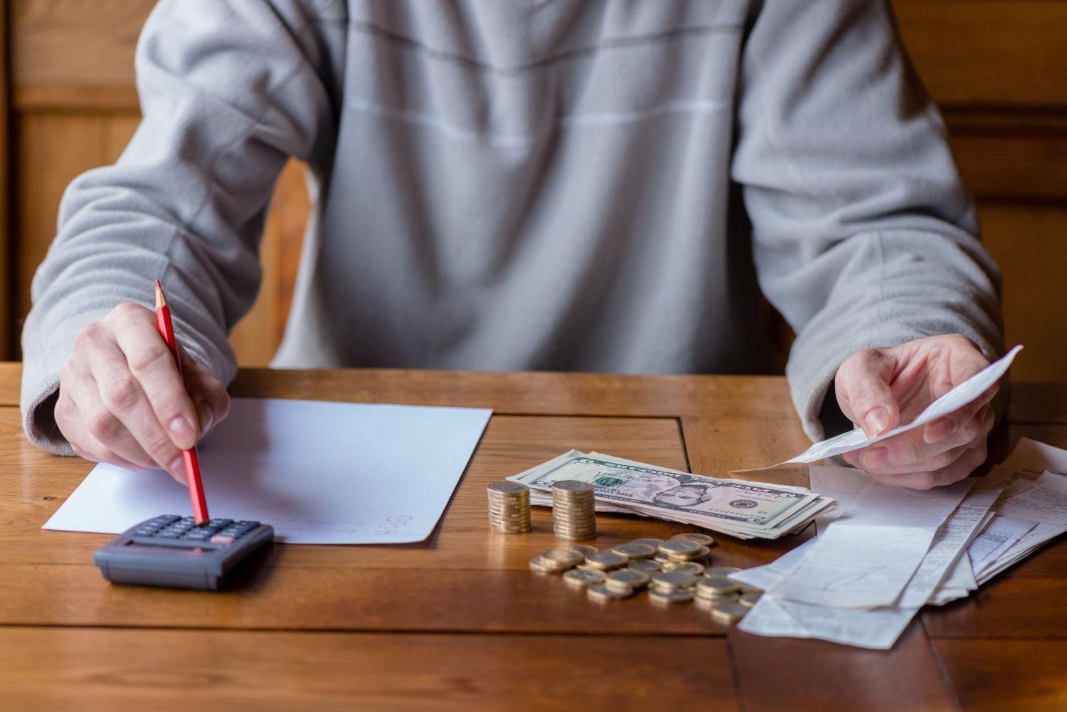 Person calculating finances at a table with money, calculator, and receipts.