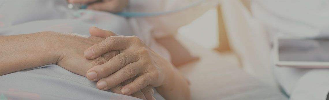 A doctor holding a patient's hand for comfort, with a stethoscope visible.