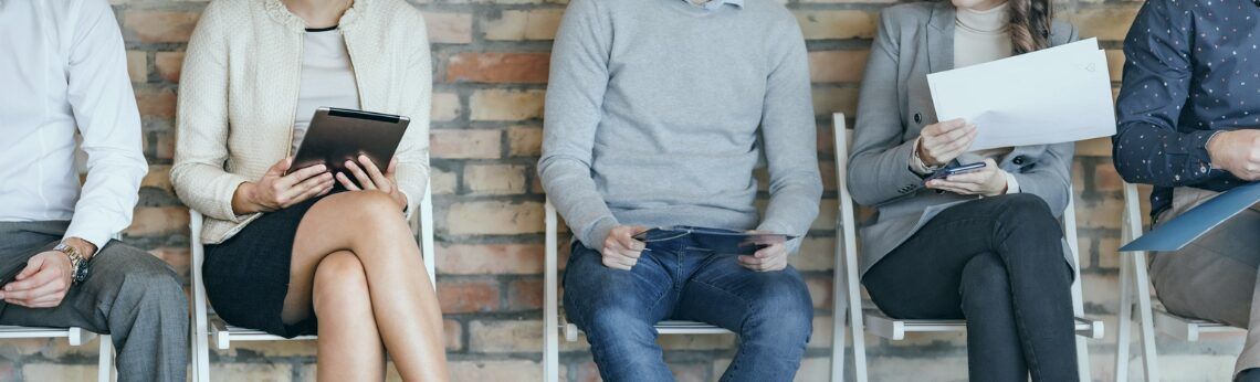 People sitting in chairs, waiting; brick wall background.
