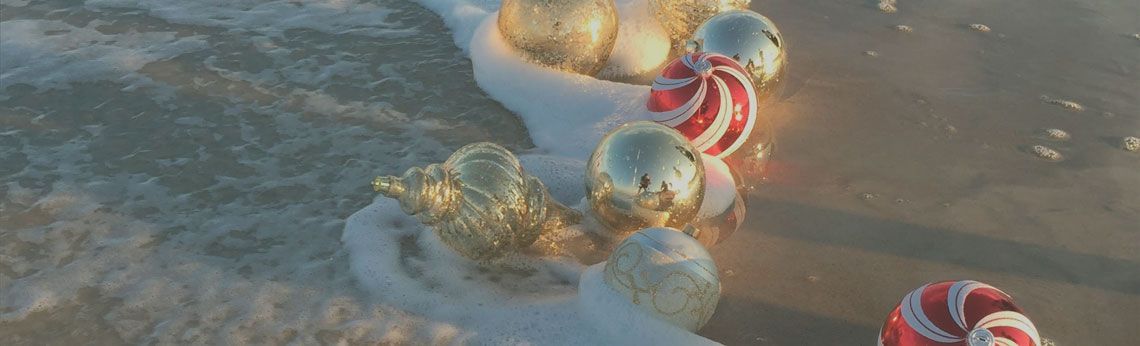 Ornaments, including gold and red-striped balls, washing up on a sandy beach, with foamy waves.