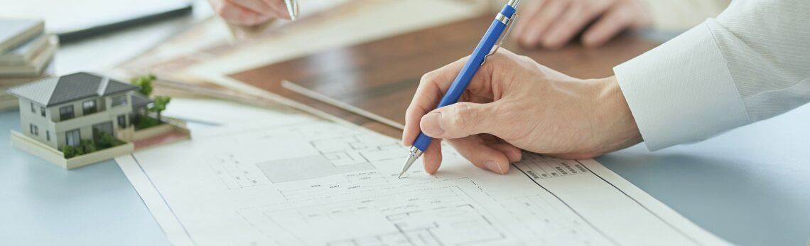 Person signing a document, with a miniature house model and papers on a desk.