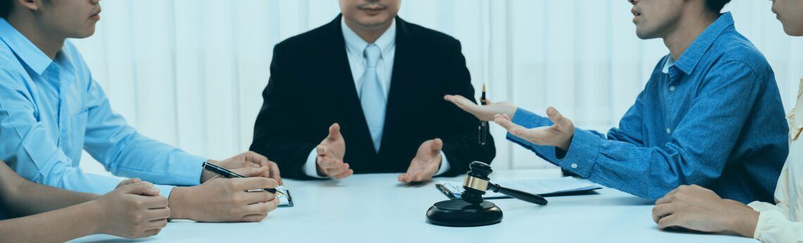 A group of people are seated around a table, one in a suit. There’s a gavel on the table.