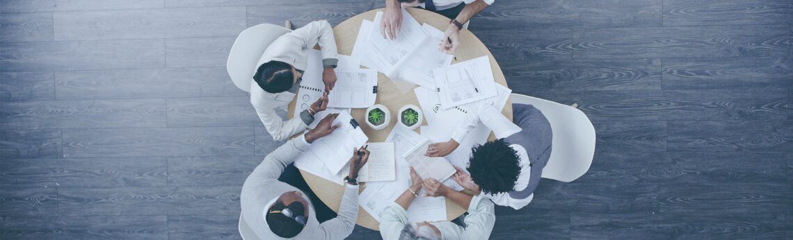 People around a table, overhead shot. White tablecloth, green objects. Gray floor.