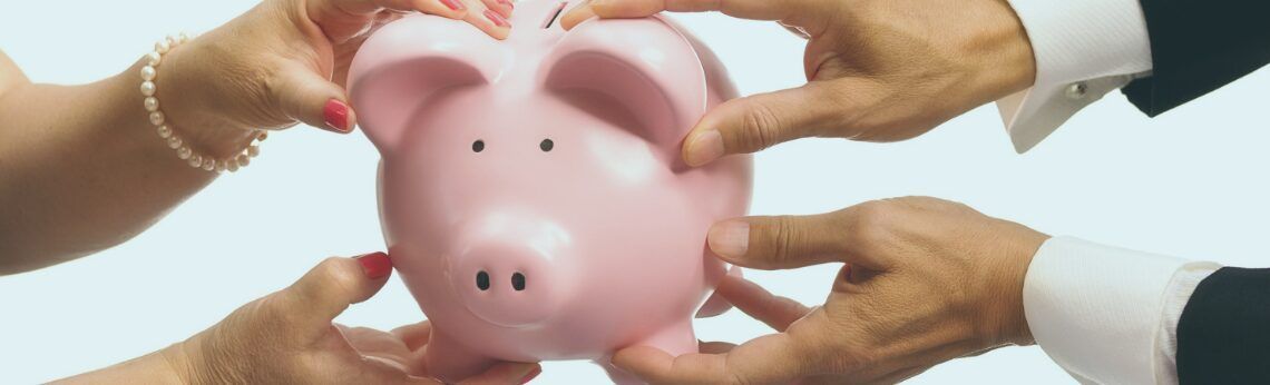 Hands of several people holding a pink piggy bank.