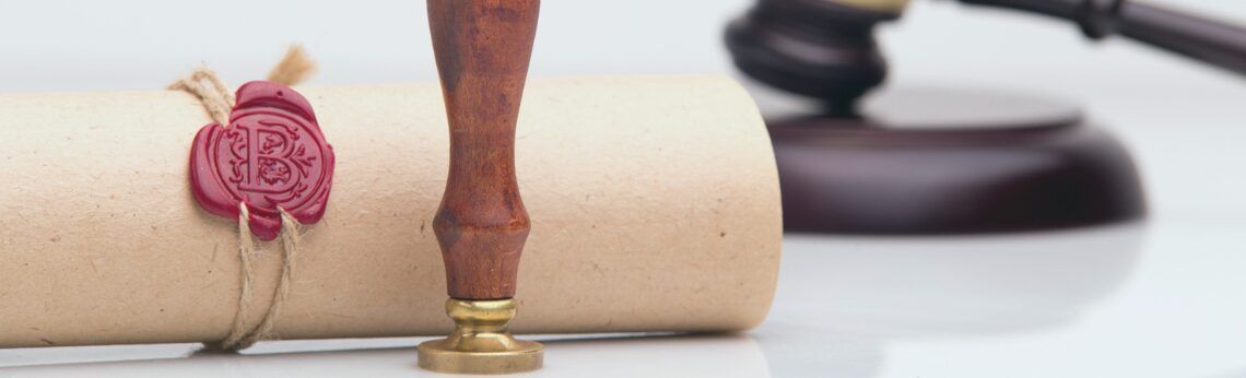 A rolled document with a wax seal, a wooden stamp, and a gavel on a white surface.
