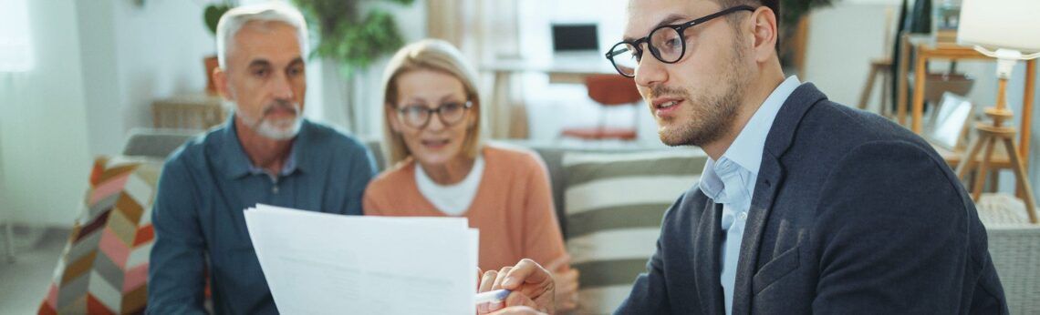 Man in glasses discusses paperwork with older couple.