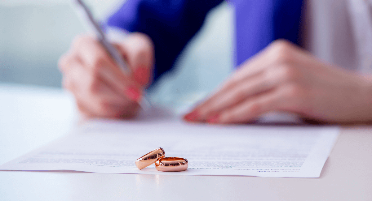 Wedding rings on divorce papers as someone signs; blue and white.