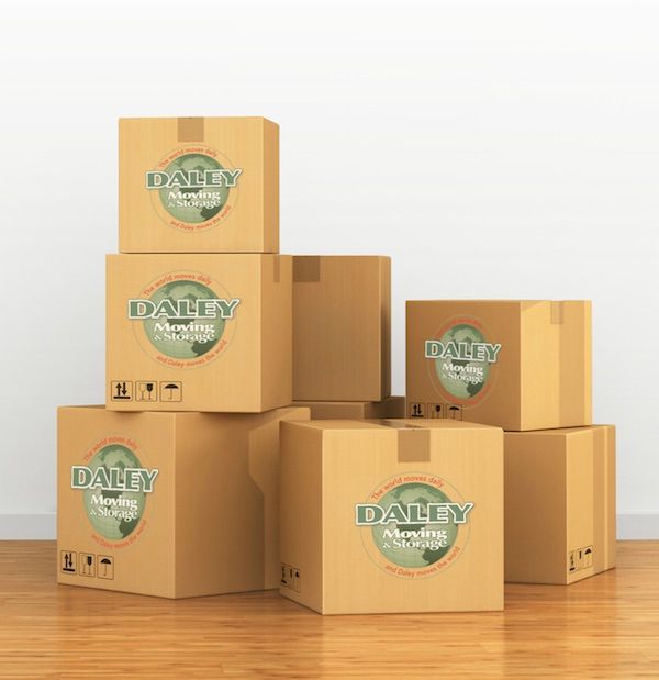 Cardboard moving boxes stacked on a wooden floor against a white wall; some boxes have a company logo.