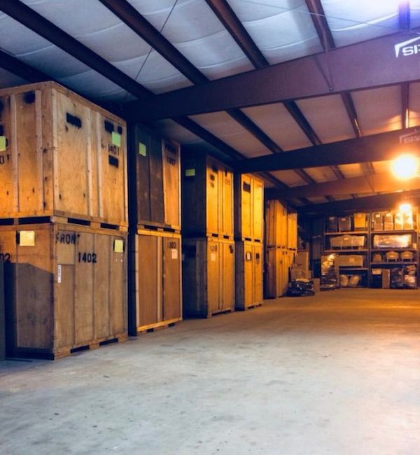 Wooden crates stacked inside a warehouse. Overhead lighting illuminates the rows of containers.