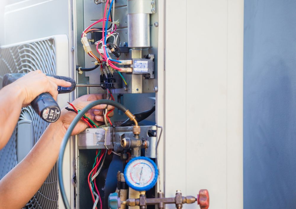 A Man Is Working on An Air Conditioner with A Screwdriver — AC Electrical & Air In Bundaberg Central, QLD