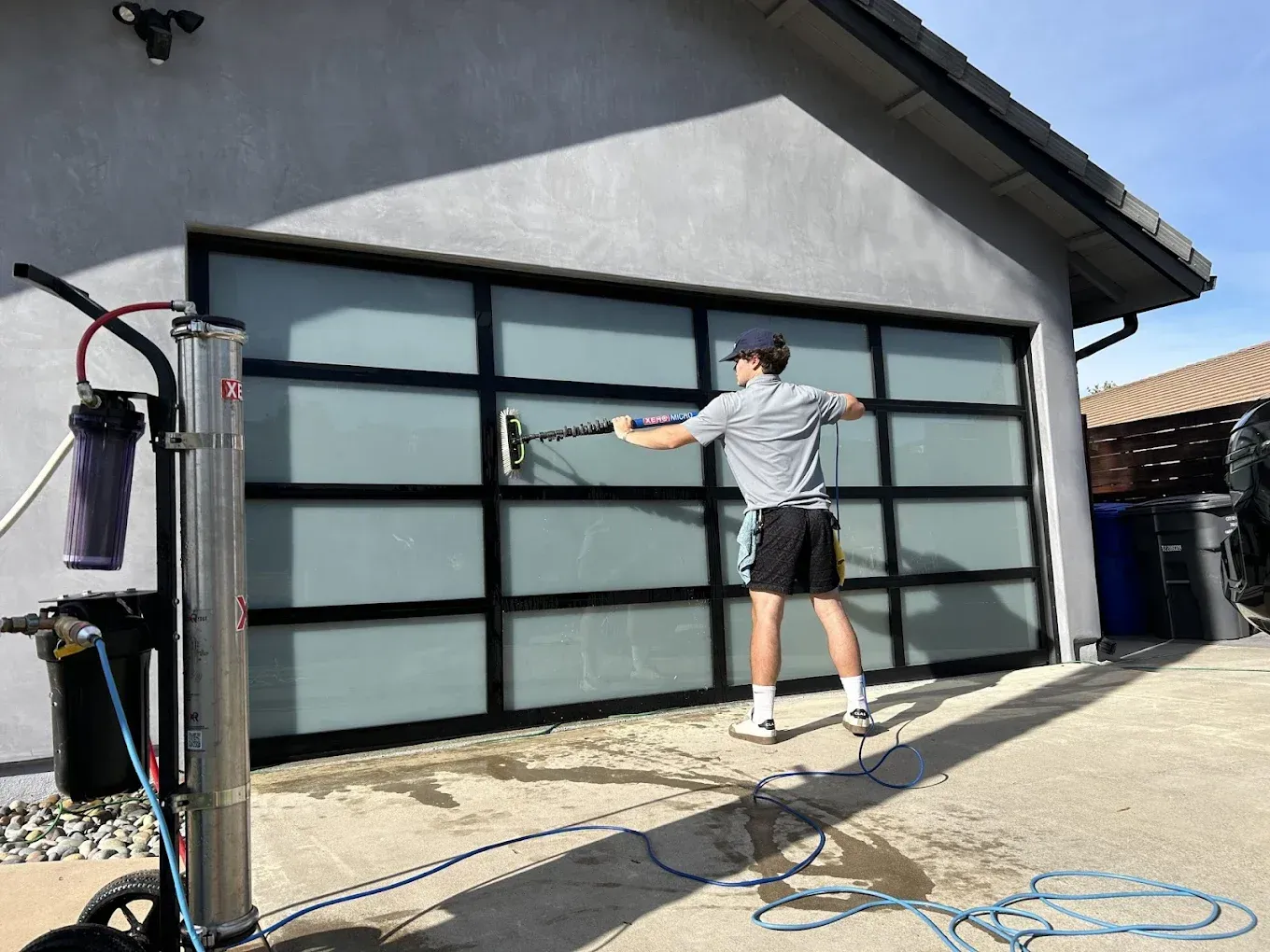 Man washing a frosted glass garage door with a squeegee; a water purification system is on the left.