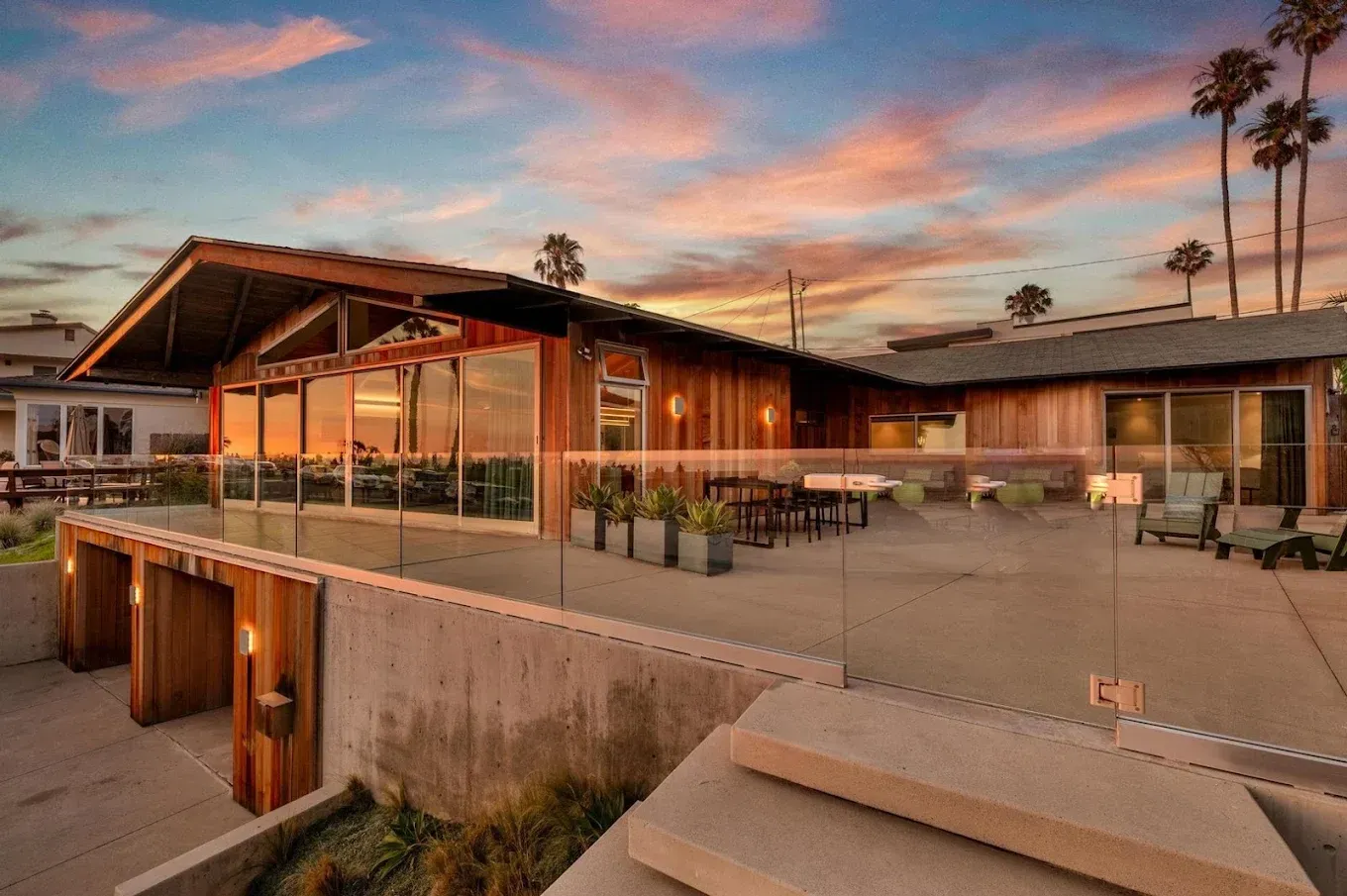 Beachfront house with wooden siding and a large deck, at sunset.