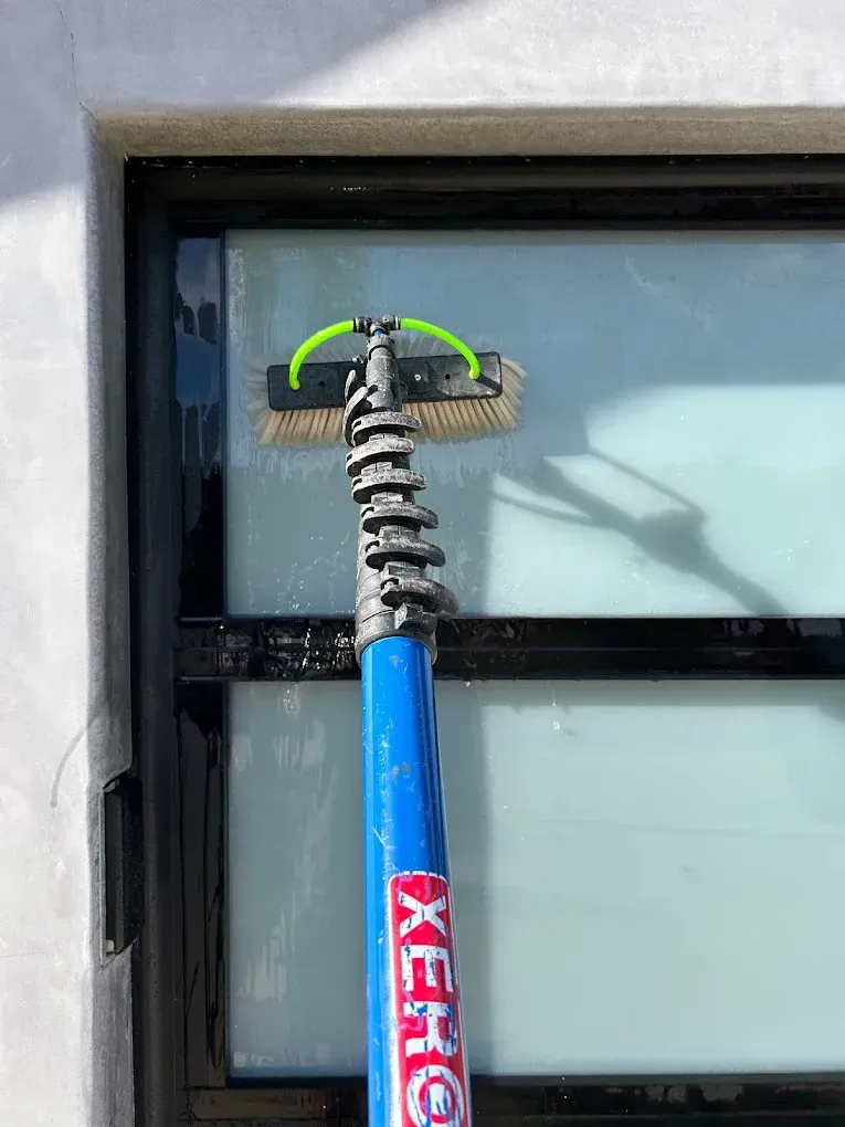A window being cleaned with a blue telescoping pole and brush.