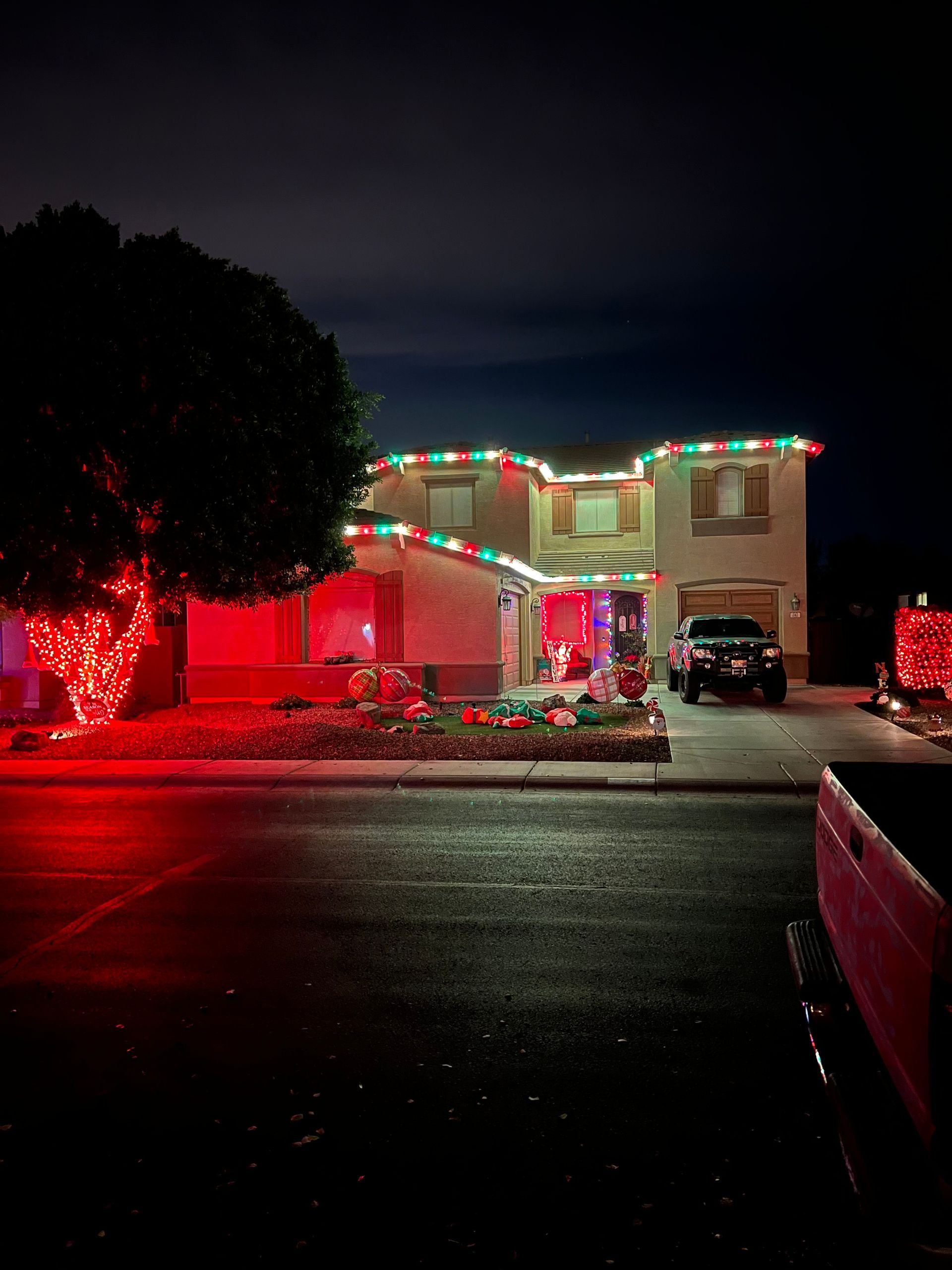 House decorated with red and green Christmas lights at night, with a tree also lit in red.