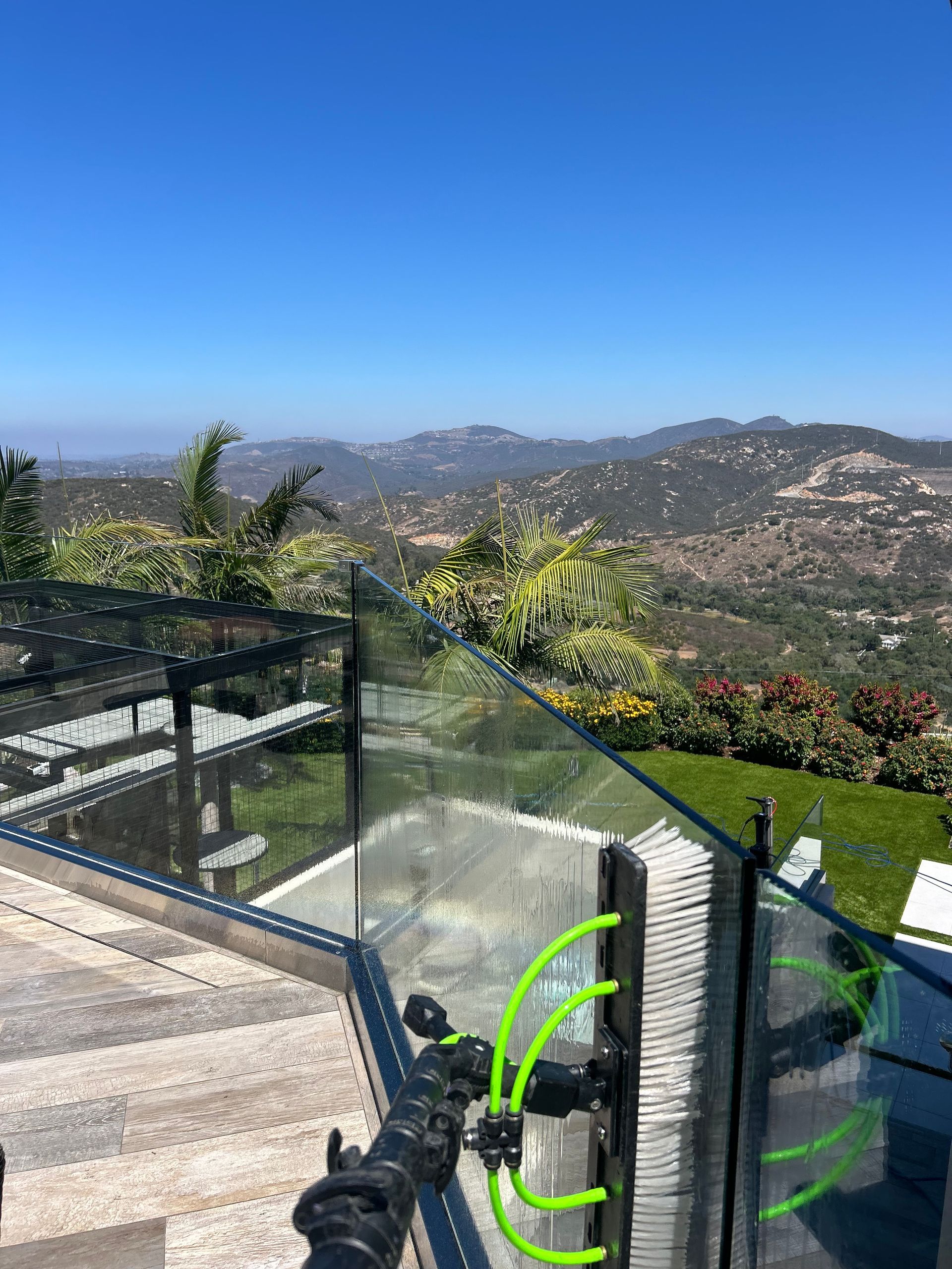Glass railing overlooks a mountainous landscape on a bright, sunny day.