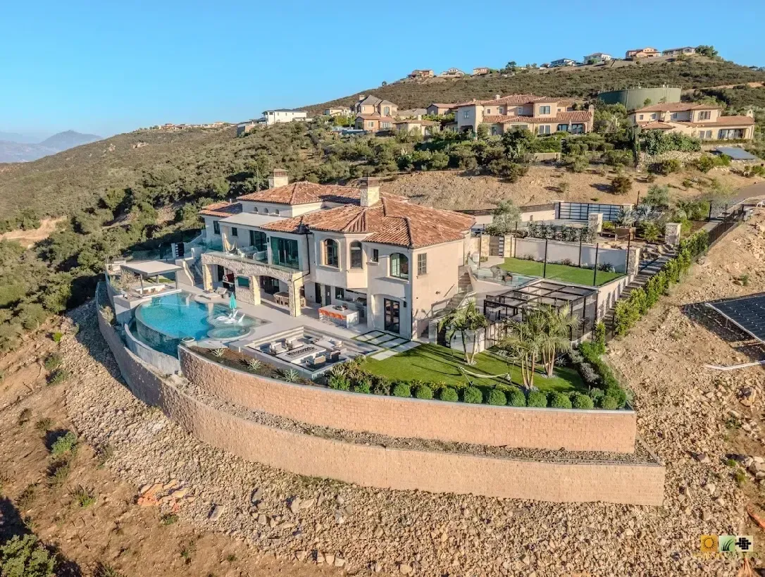 Luxurious hillside home with a pool, overlooking a valley with other homes, under a clear sky.