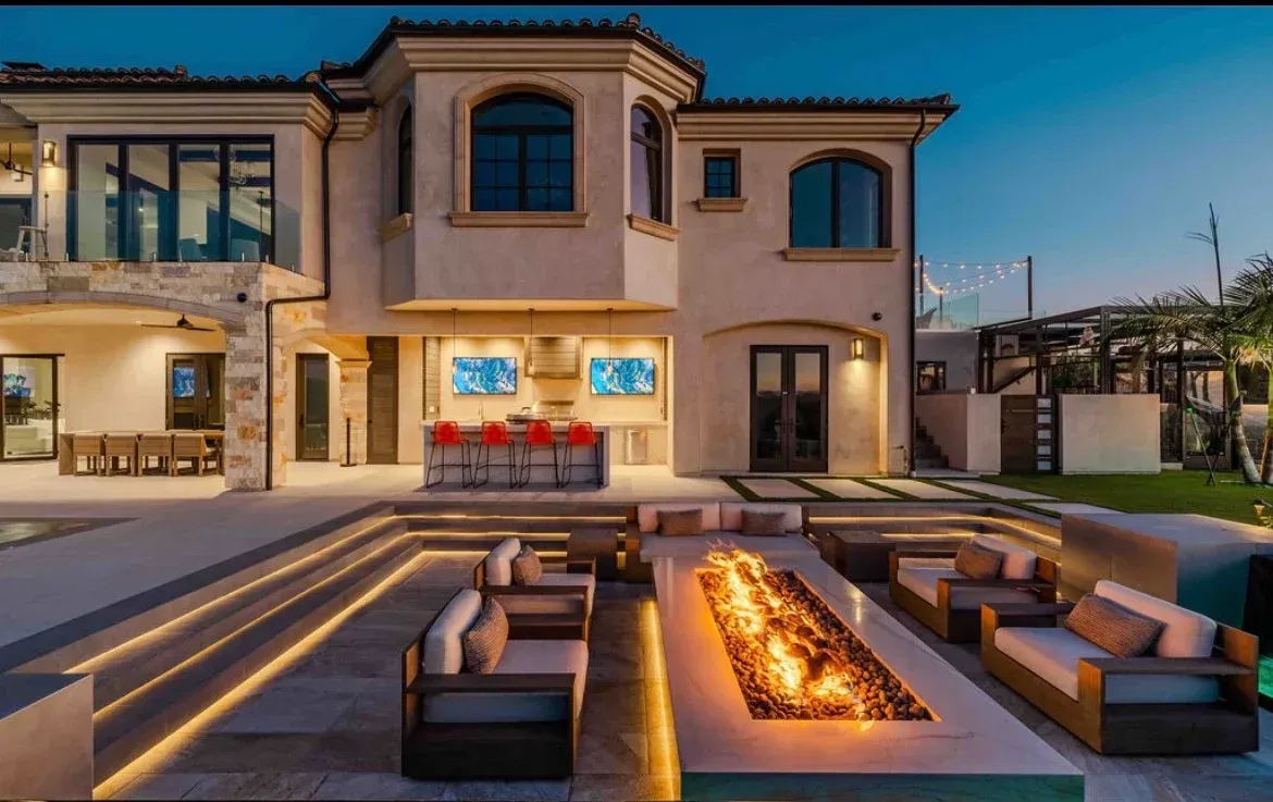 Luxury home exterior with lit patio, outdoor bar, and fire pit lounge area in Rancho Santa Fe