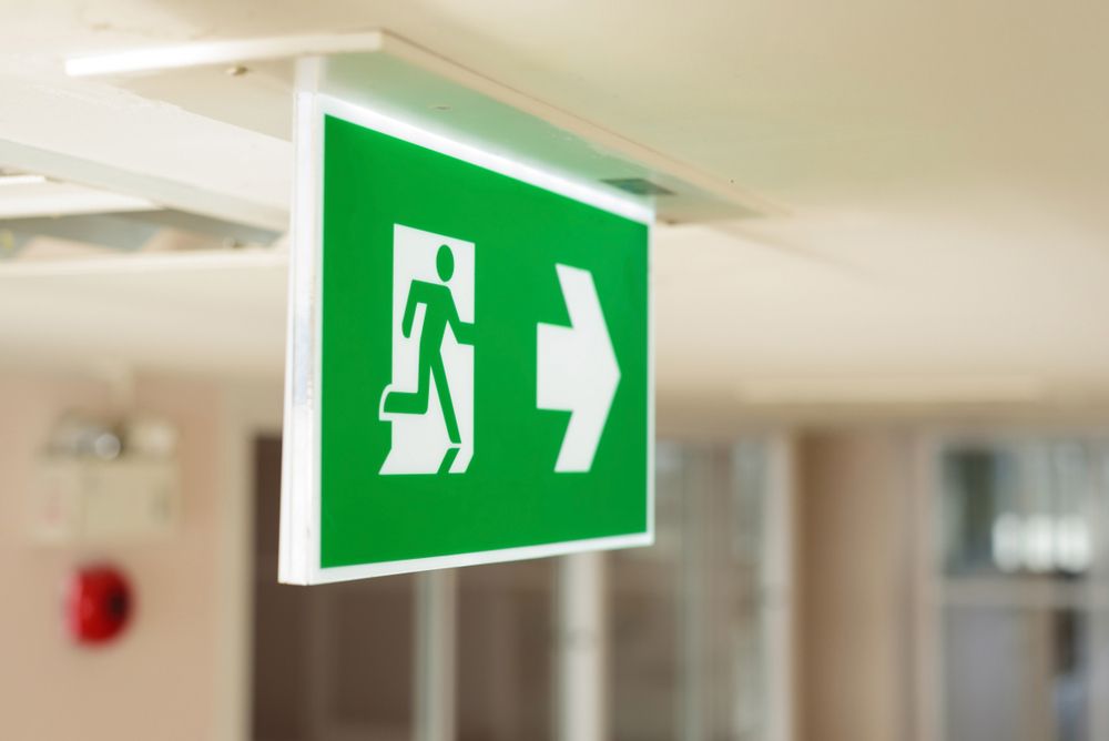 A Green Exit Sign Is Hanging From The Ceiling In A Hallway — Northern Testing in Winnellie, NT