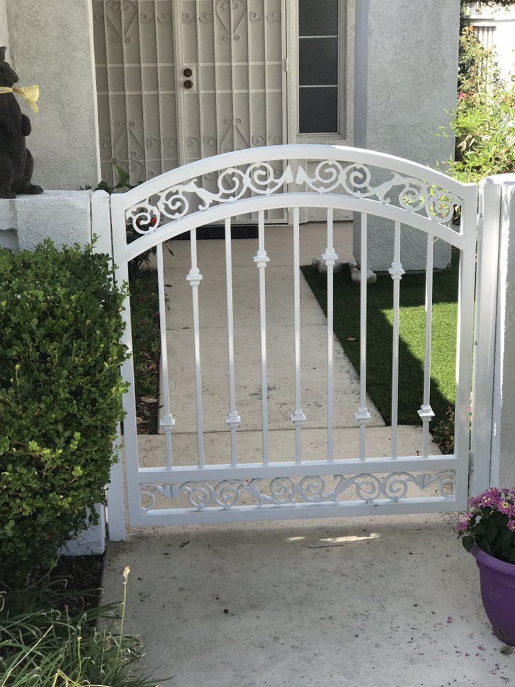 White wrought-iron gate in front of a building entrance with a small lawn.