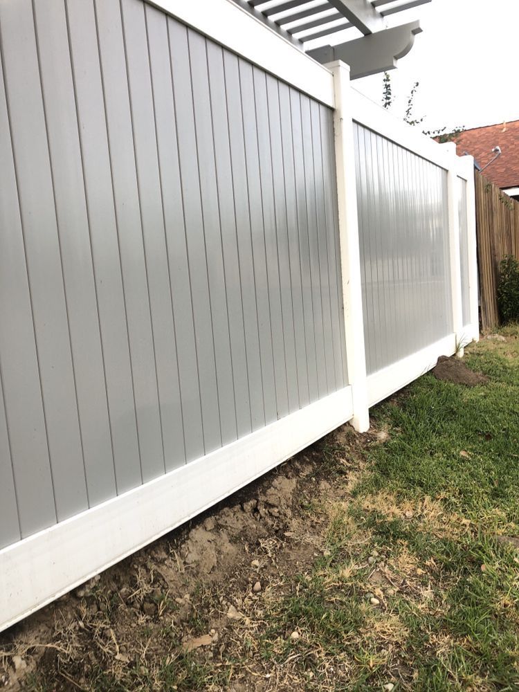 Gray and white vertical-slat fence alongside green grass and dirt.