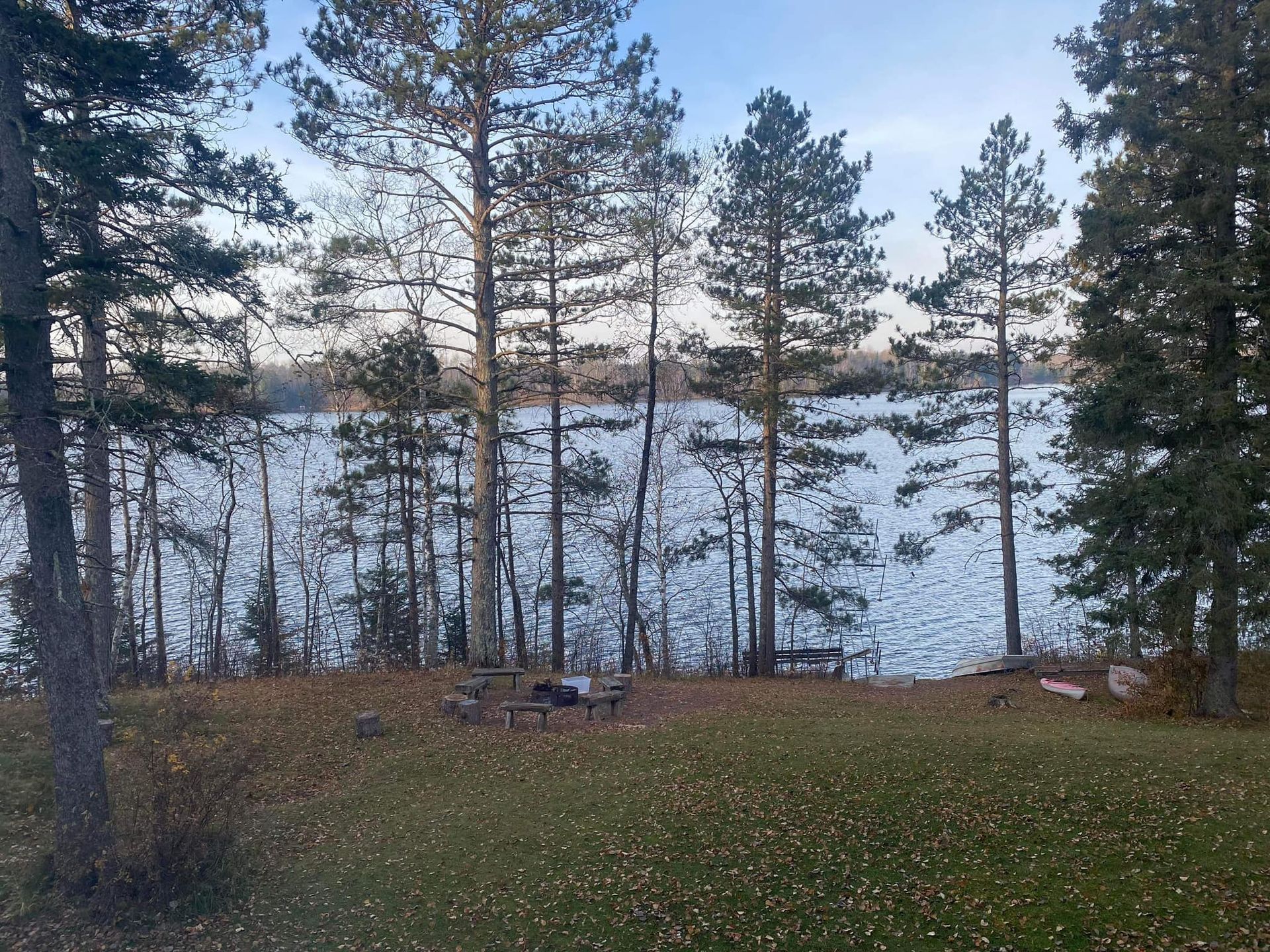 A lake surrounded by trees and grass with a fire pit in the foreground