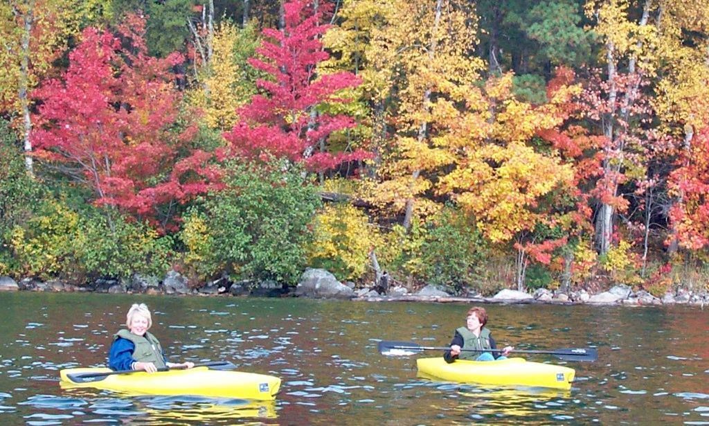Two people in yellow kayaks on a lake with trees in the background