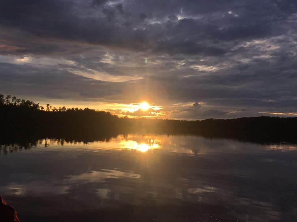 The sun is setting over a lake with trees in the background.