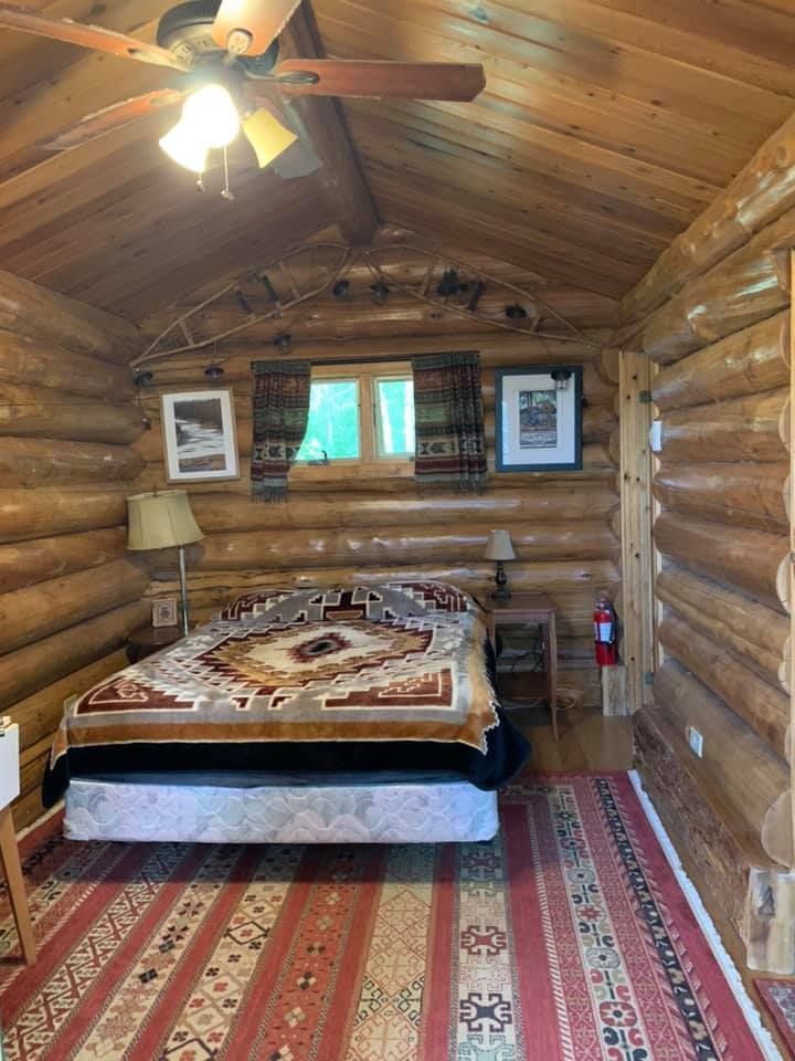 A bedroom in a log cabin with a bed and a ceiling fan.