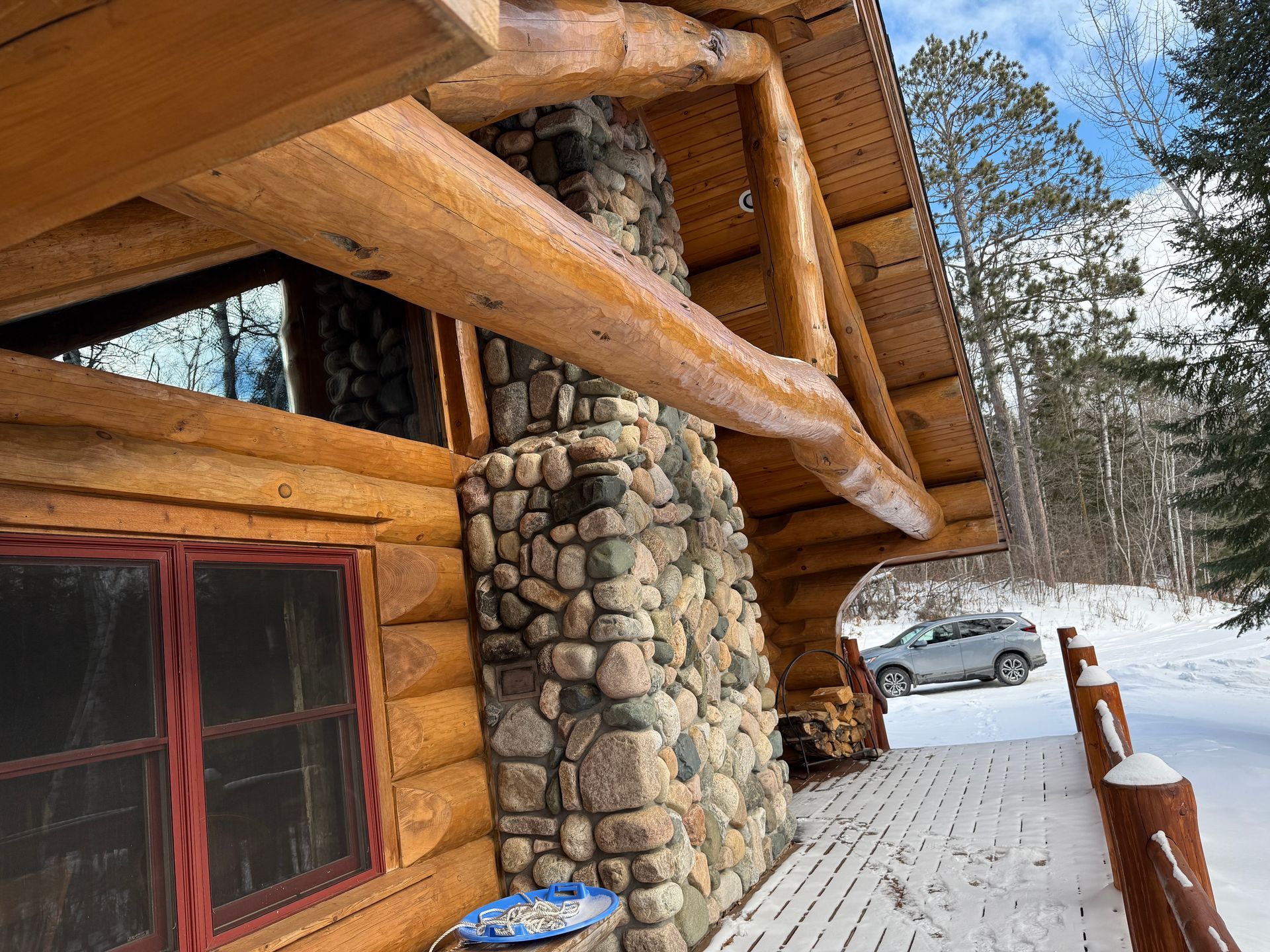 A log cabin with a stone chimney and a car parked in the snow.