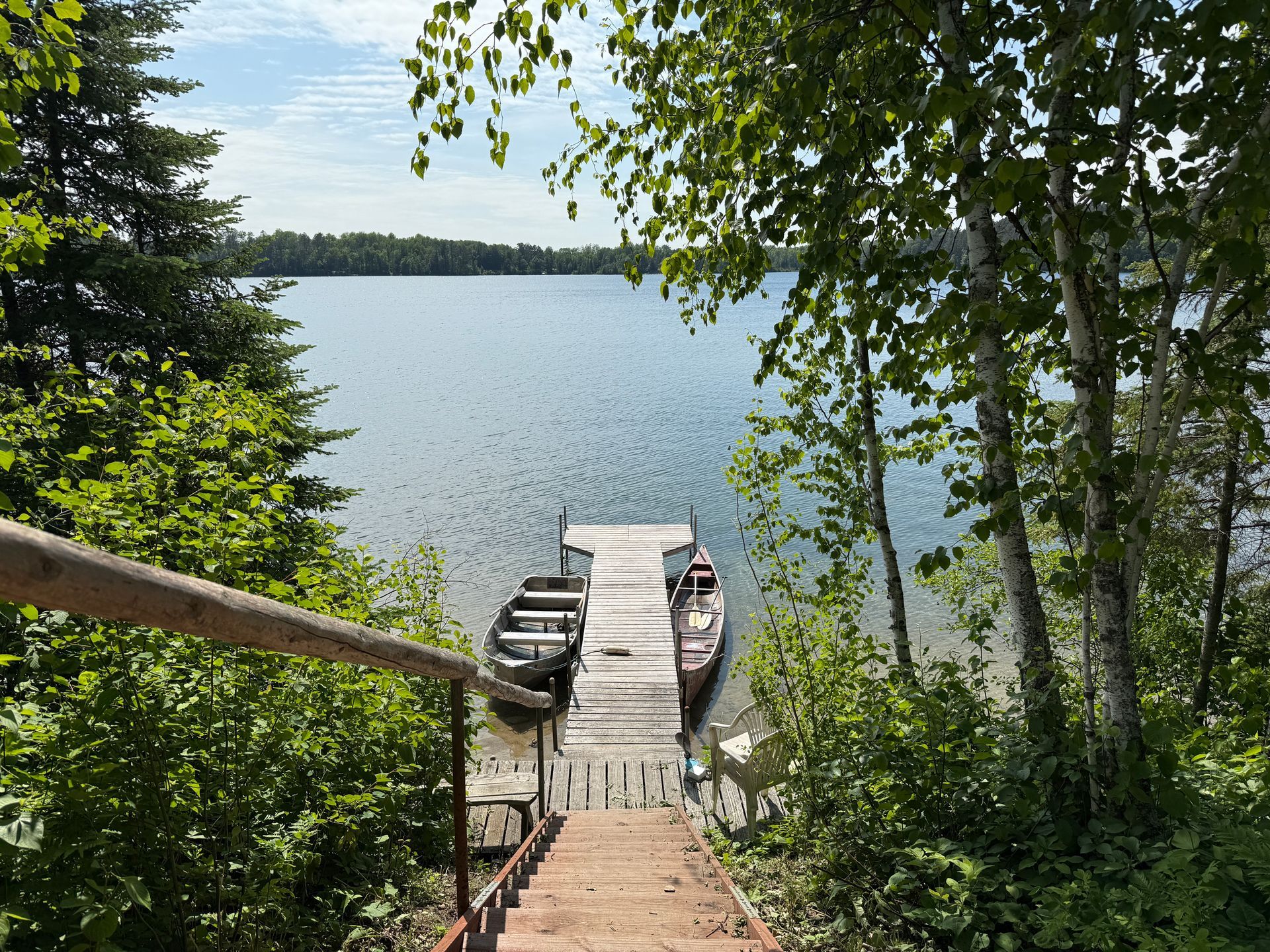A wooden dock with boats docked at the end of it surrounded by trees.