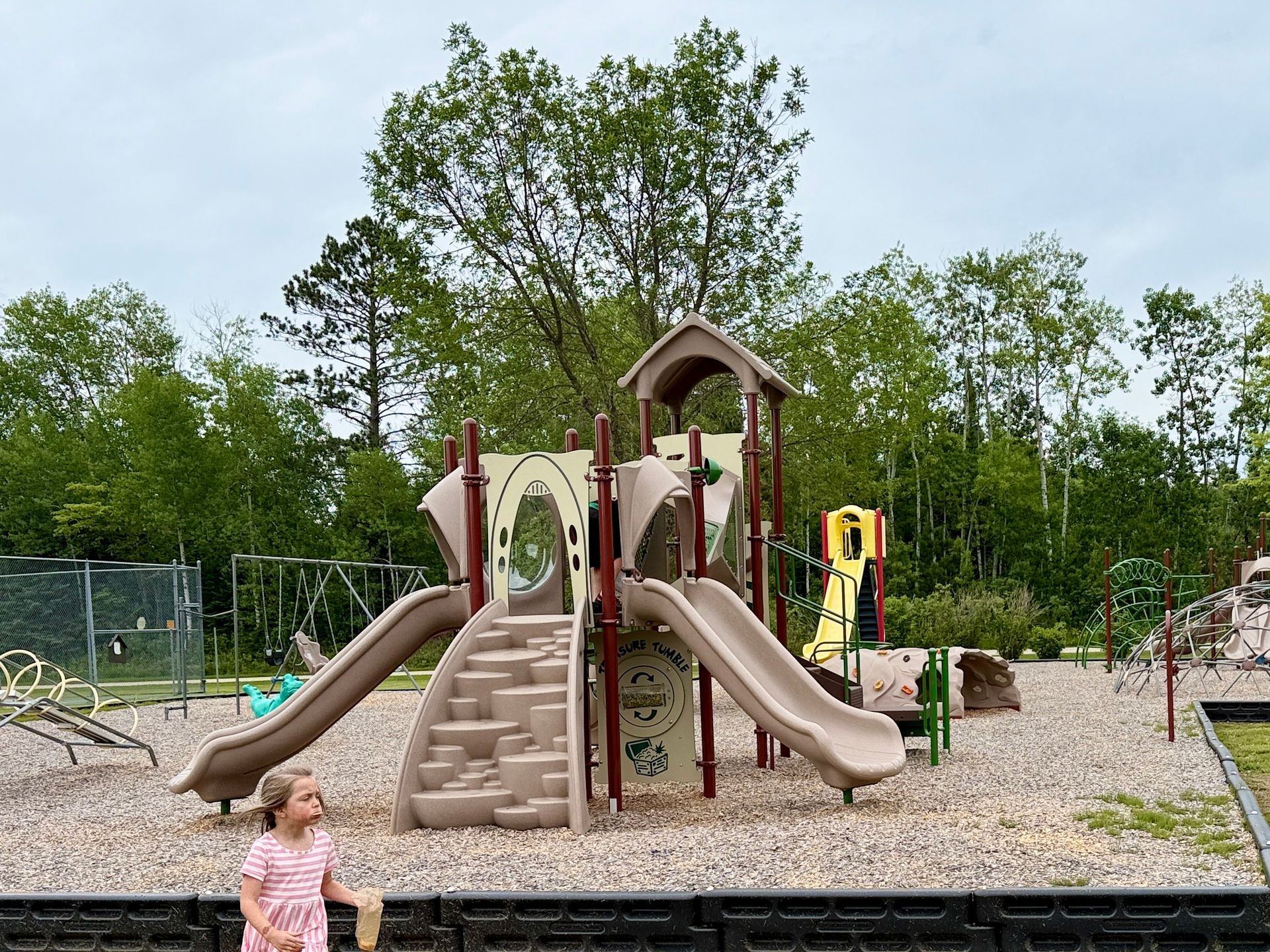 A little girl is standing in front of a playground.
