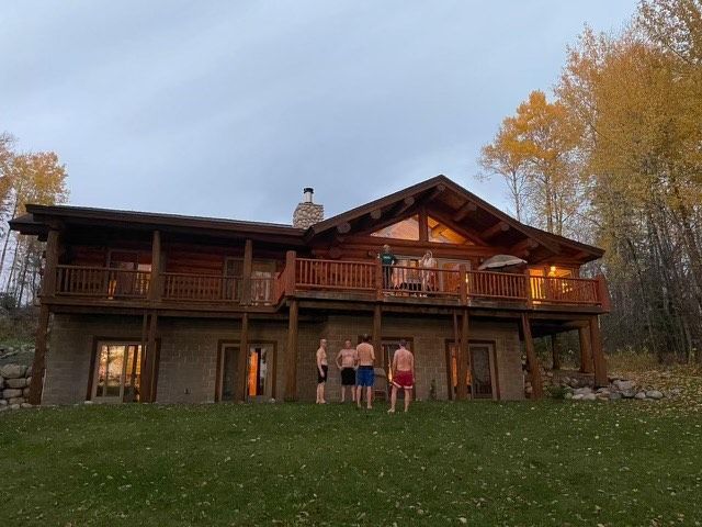 A group of men are standing in front of a large log cabin.