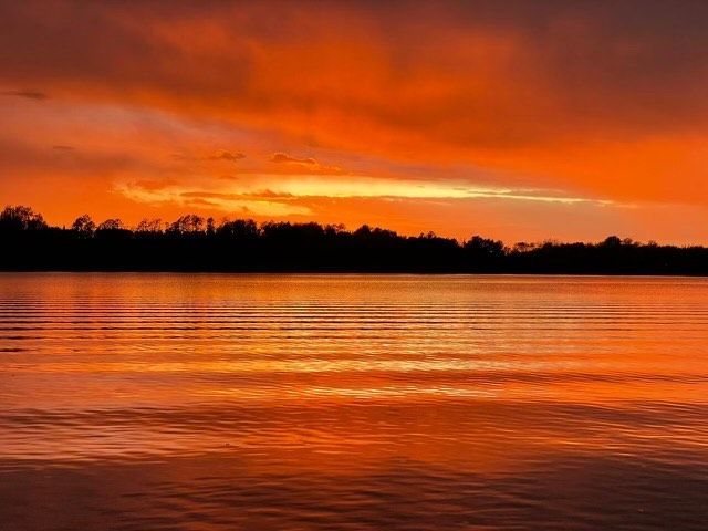 A sunset over a lake with trees in the background