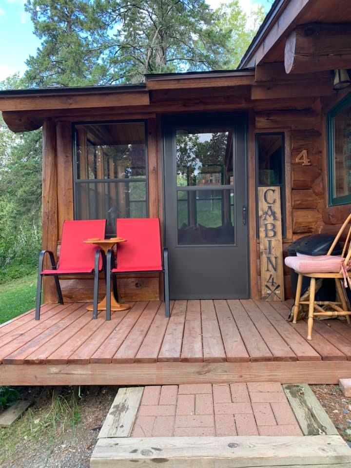 A wooden cabin with two red chairs and a table on the deck.