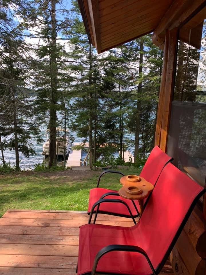 Two red chairs are sitting on a wooden deck overlooking a lake.