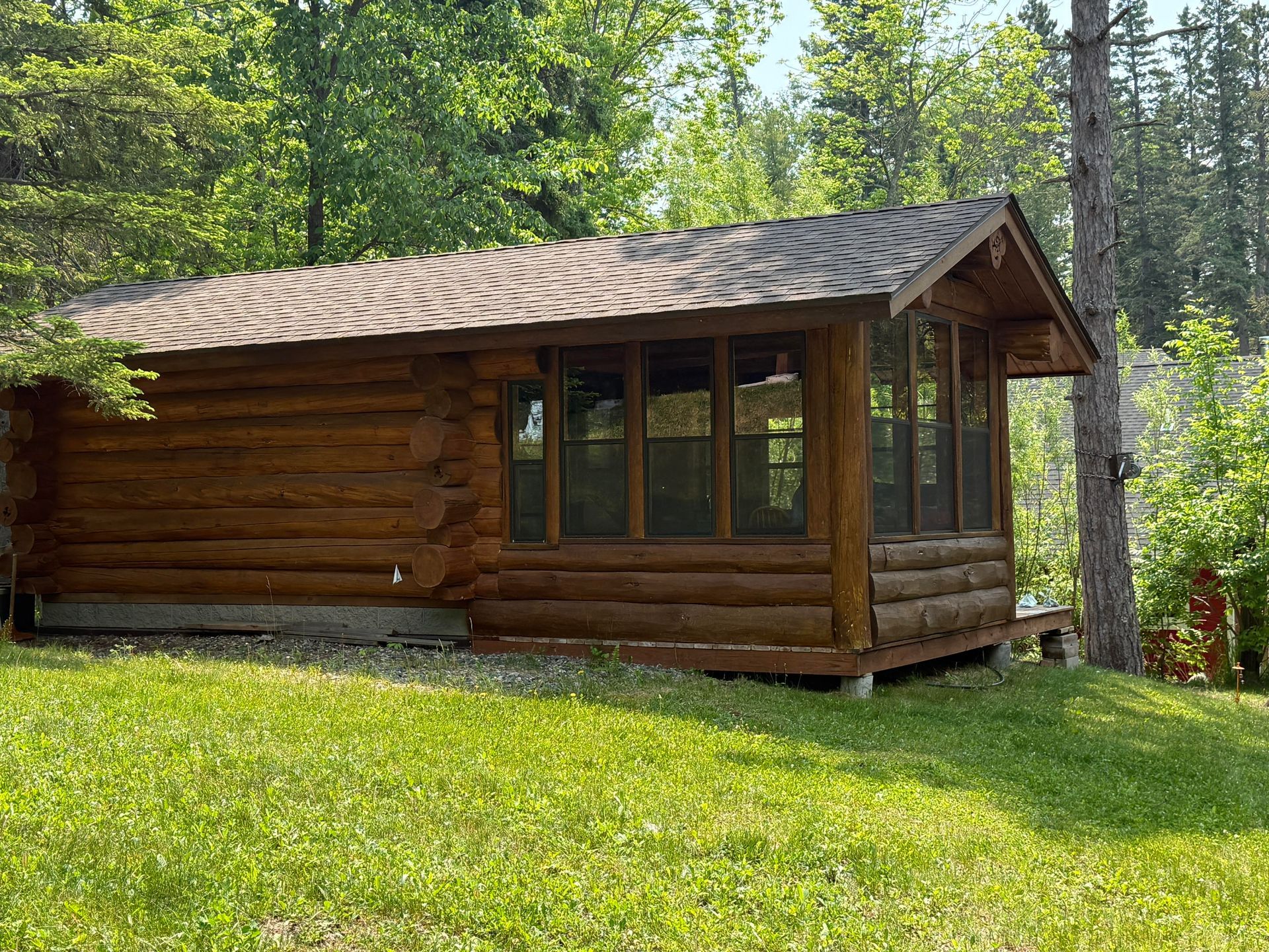 A log cabin with a screened in porch is sitting on top of a lush green field.