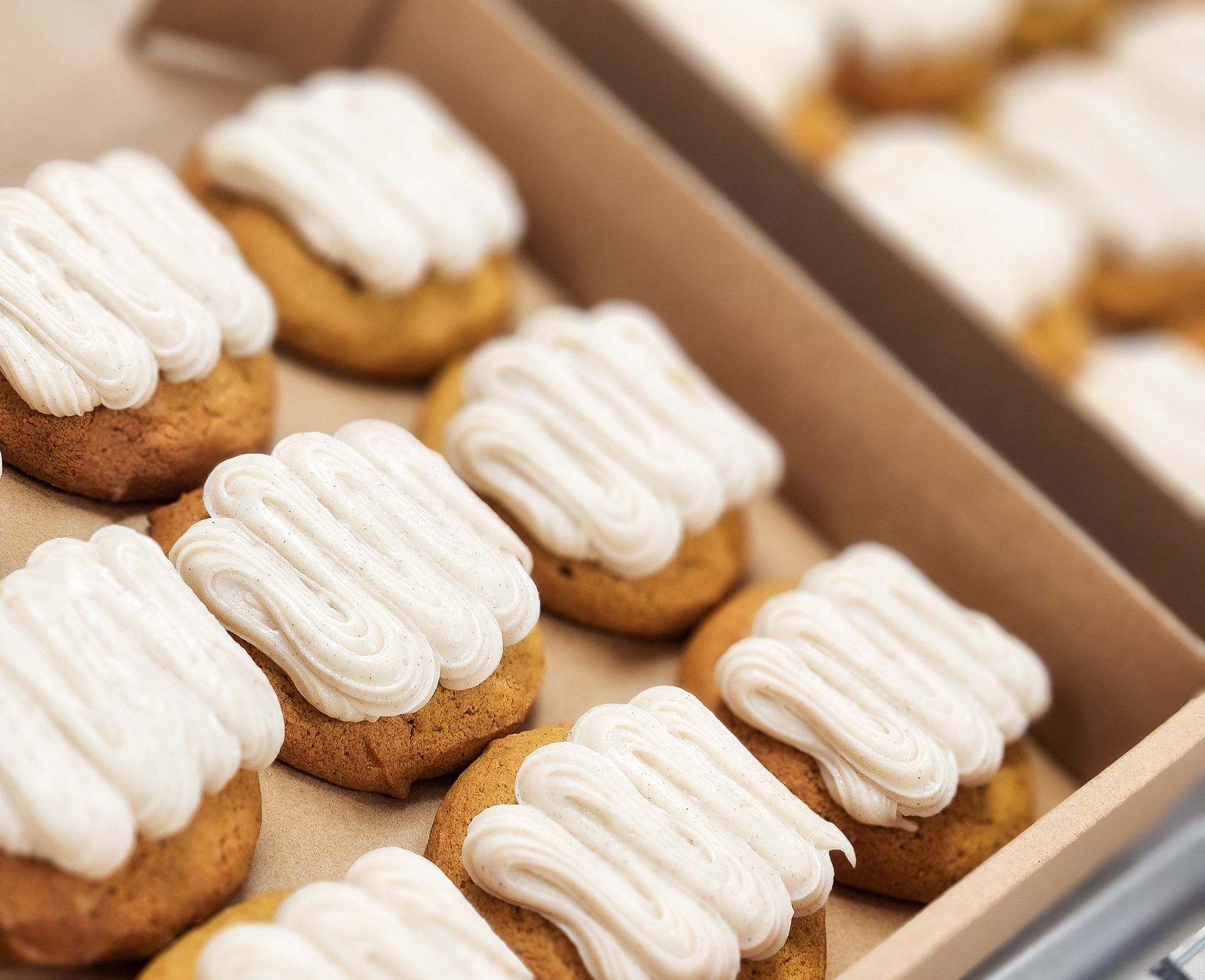 A tray of golden-brown cookies topped with white frosting in a cardboard box.