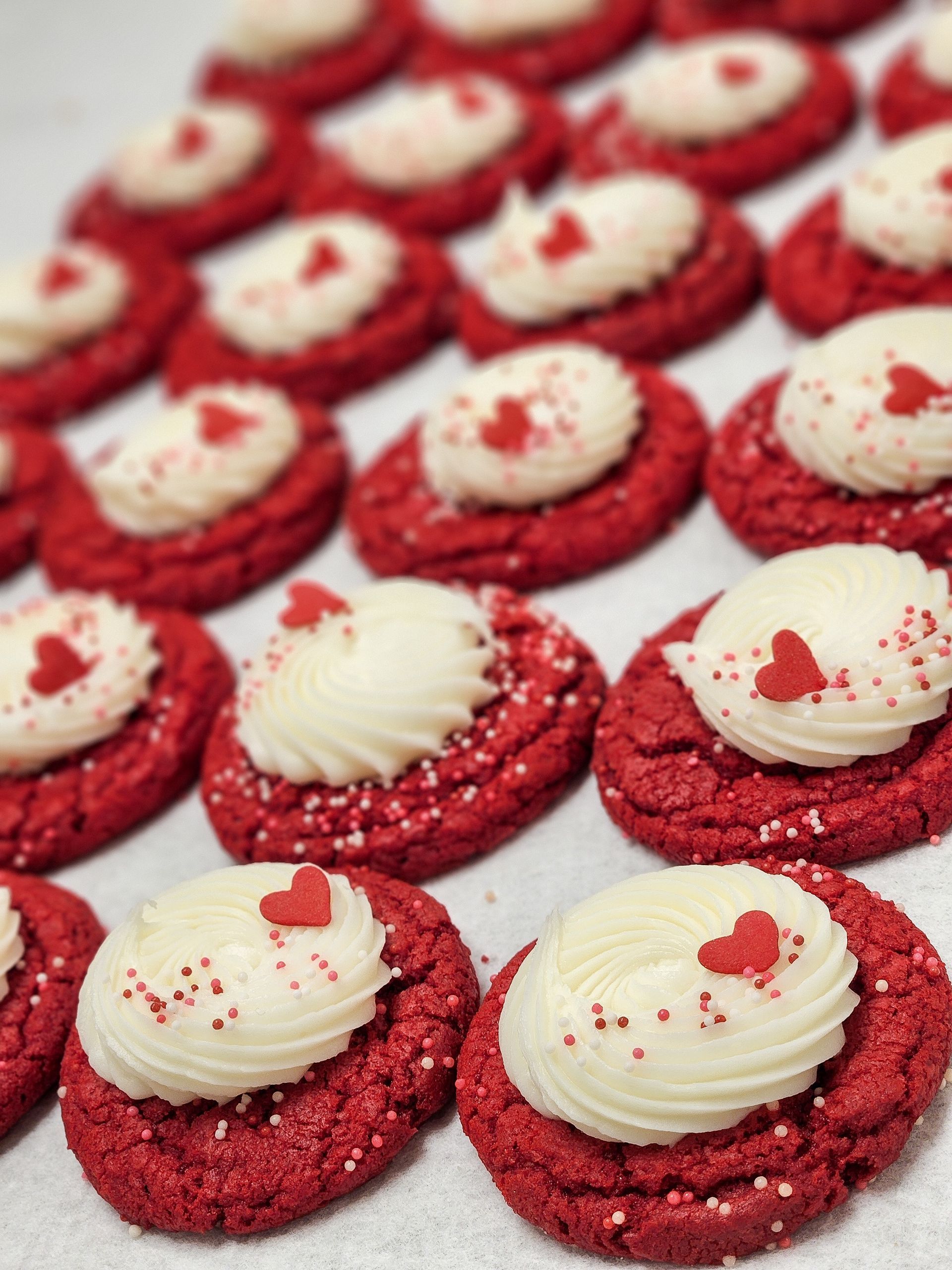 Three frosted sugar cookies with Christmas sprinkles on a cooling rack, with holiday decorations.