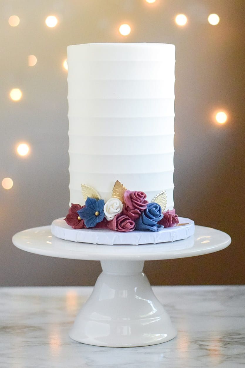 A white cake with flowers on top of it on a white cake stand.