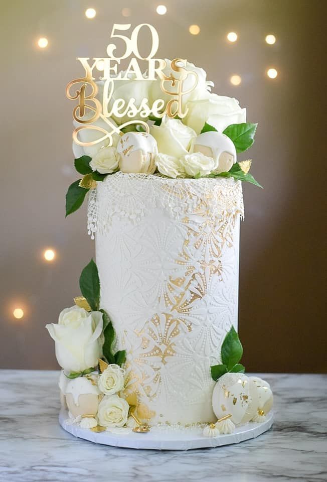 A white cake with white roses and leaves on it is on a table.