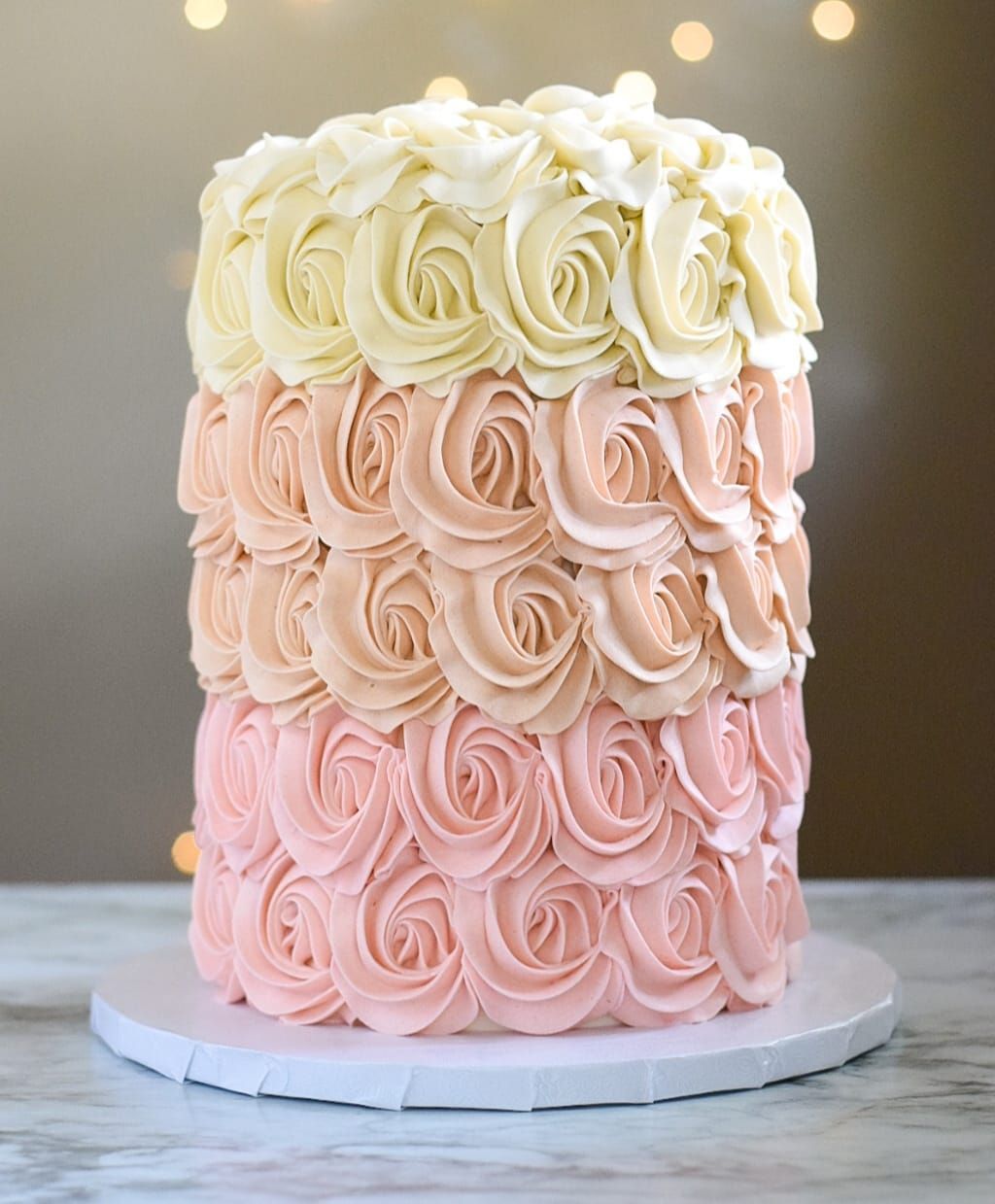A pink and white cake with roses on it is sitting on a table.