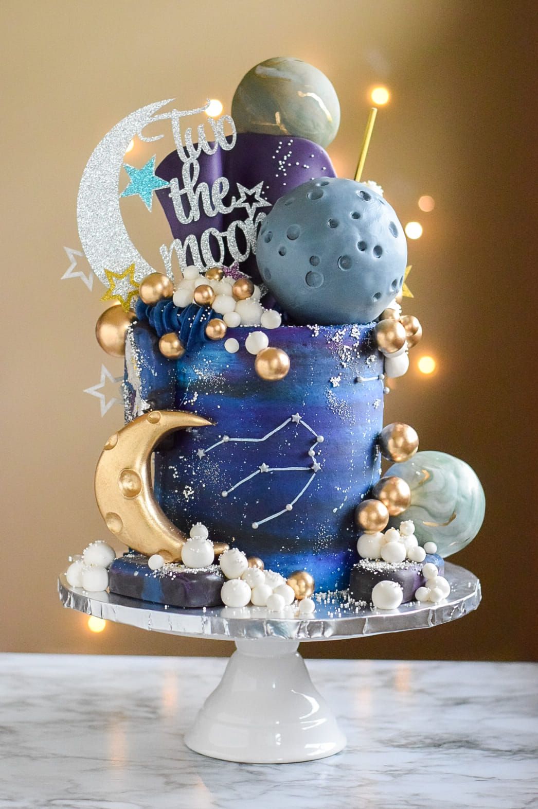 A cake with a crescent moon on top of it is on a cake stand.