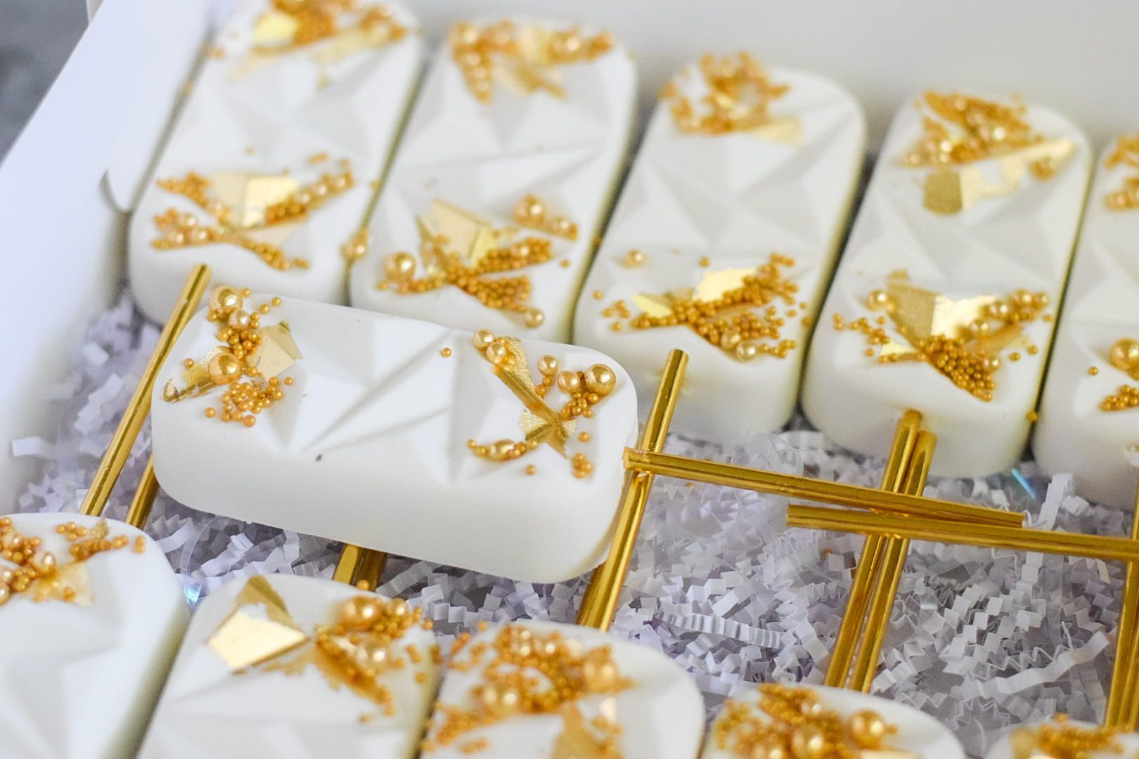 A box of white and gold ice cream bars with gold sprinkles.