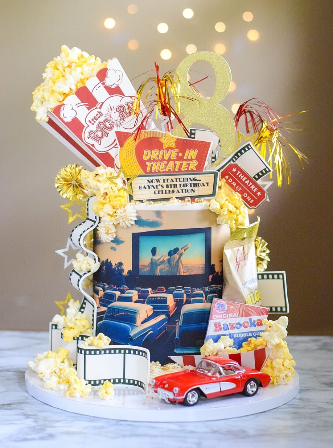 A cake decorated to look like a drive-in theater with popcorn and a car.