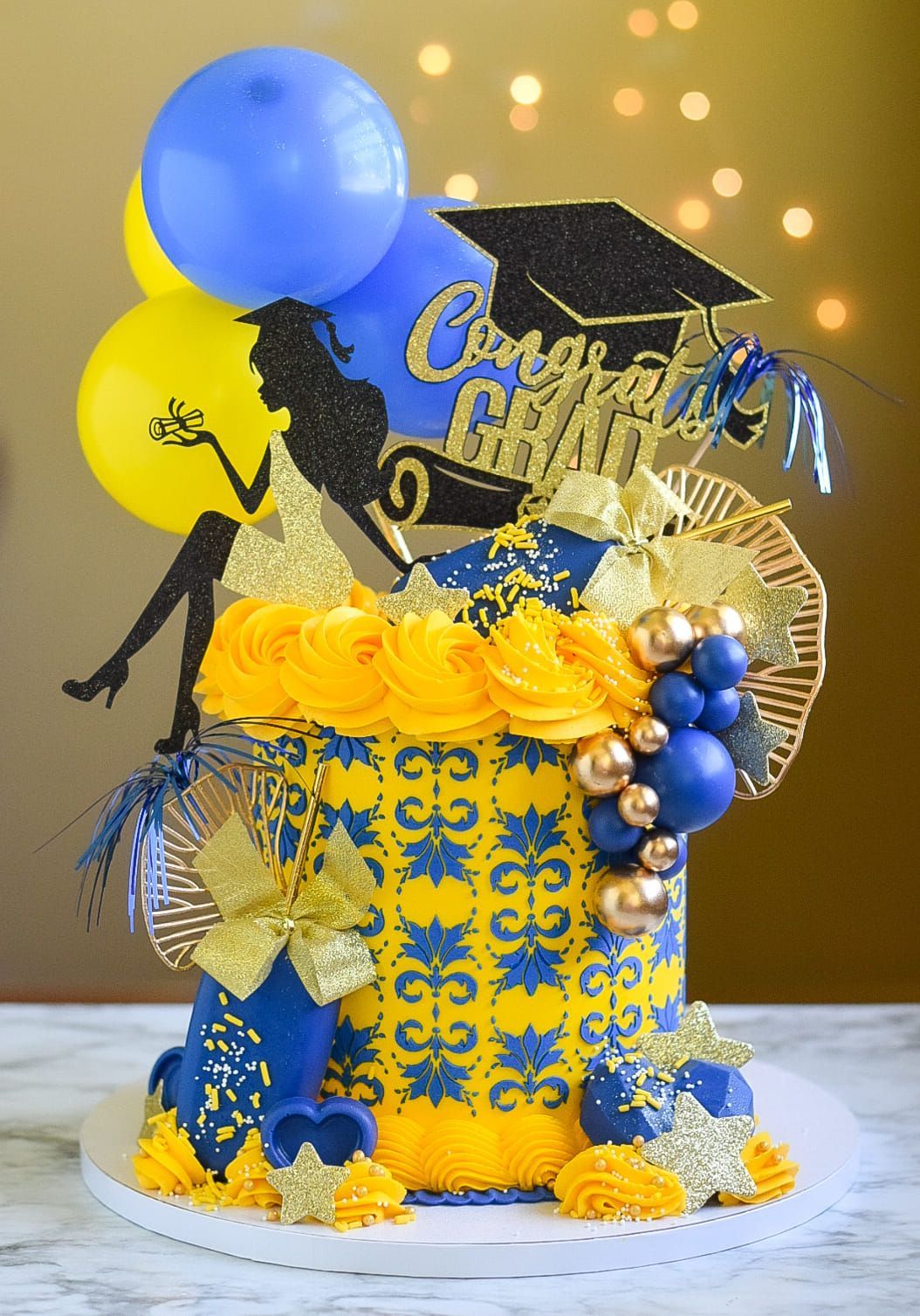 A blue and yellow cake with balloons and a graduation cap on top.