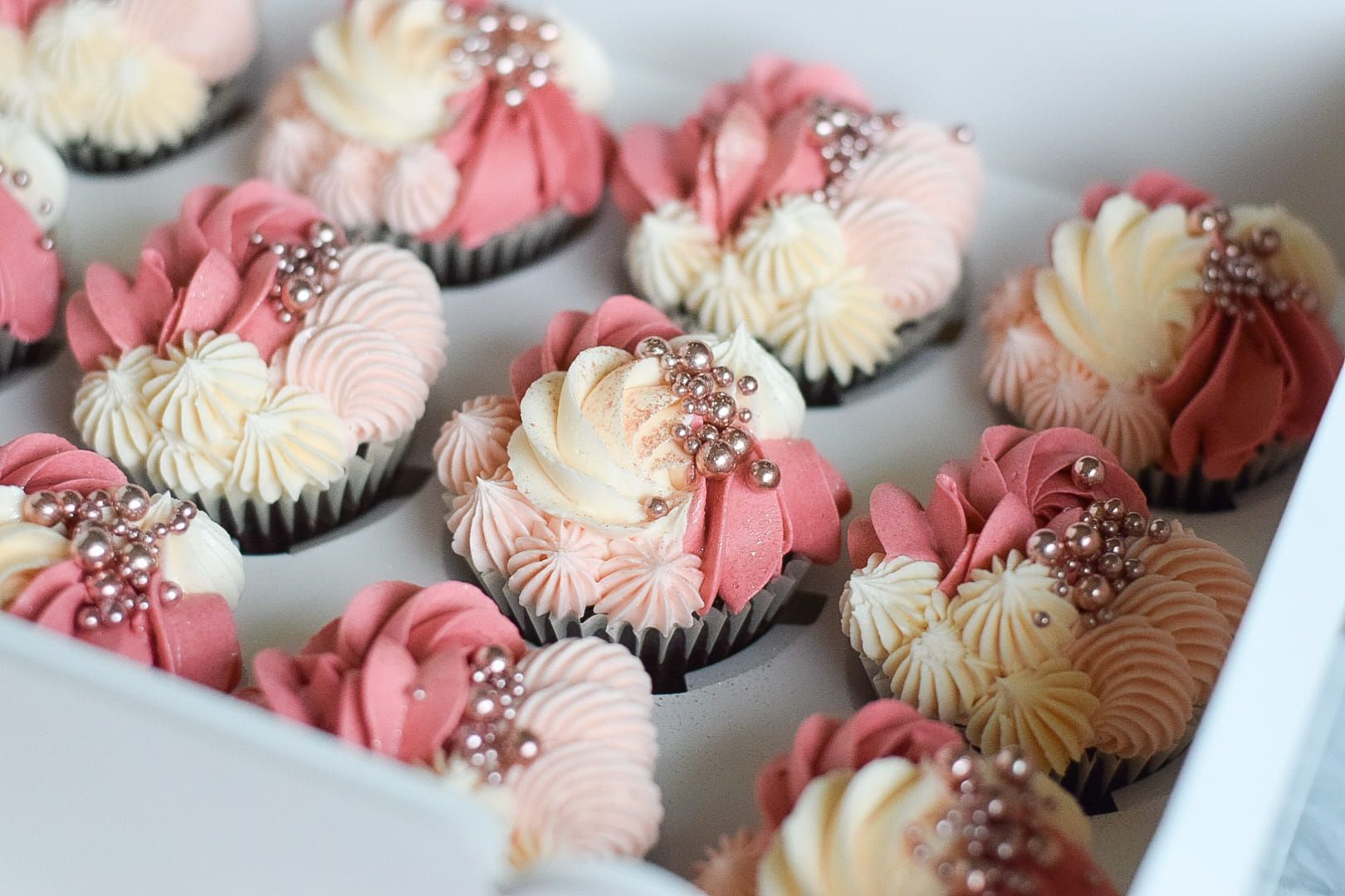 A box of cupcakes with pink and white frosting and sprinkles.